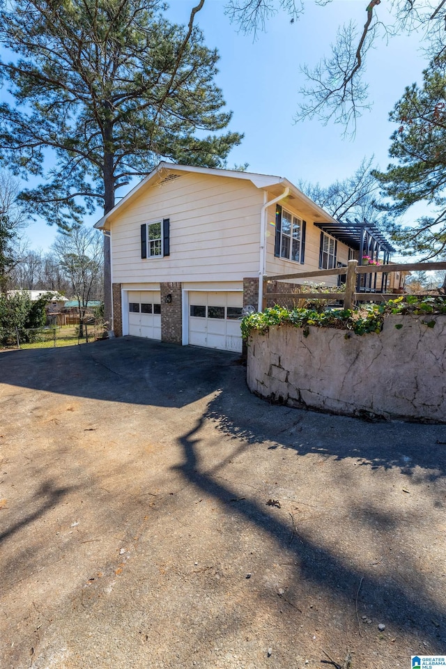 view of side of property featuring brick siding, driveway, an attached garage, and fence