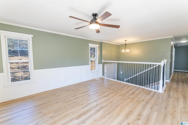 unfurnished room with a wainscoted wall, ceiling fan with notable chandelier, wood finished floors, and ornamental molding