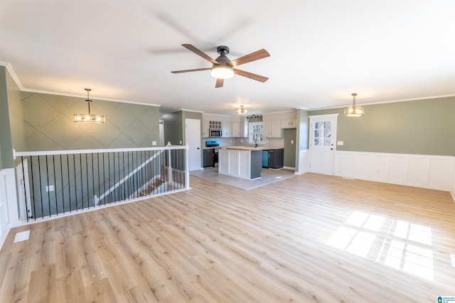 interior space with light wood-type flooring, a wainscoted wall, crown molding, and ceiling fan with notable chandelier