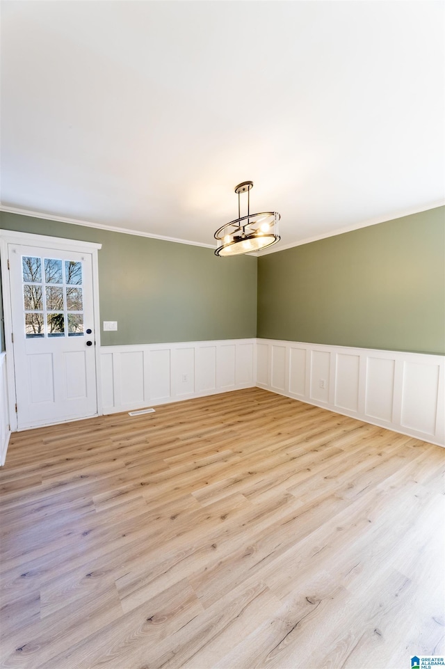 spare room featuring a wainscoted wall, light wood-type flooring, and ornamental molding