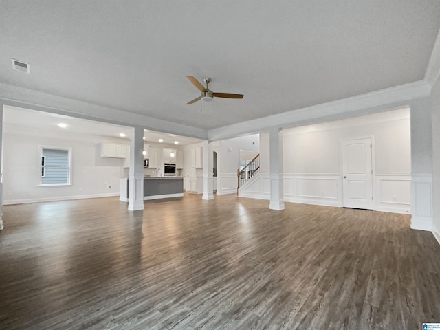 unfurnished living room featuring stairway, visible vents, ceiling fan, dark wood-type flooring, and a decorative wall