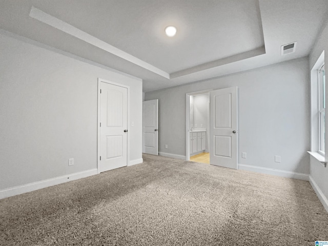 unfurnished bedroom featuring baseboards, a tray ceiling, light carpet, and visible vents