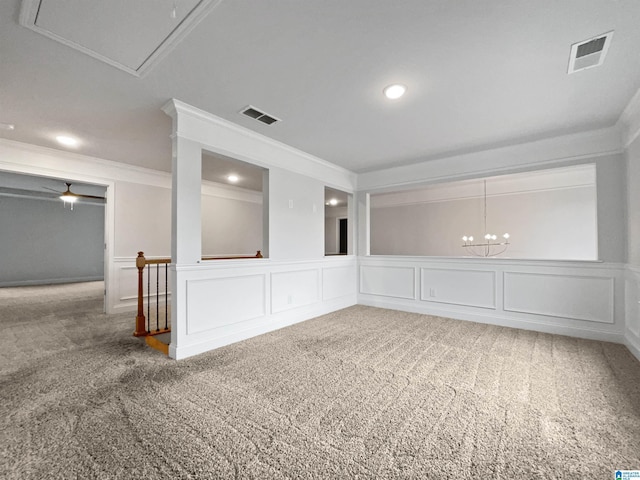 carpeted empty room with visible vents, attic access, crown molding, and a decorative wall