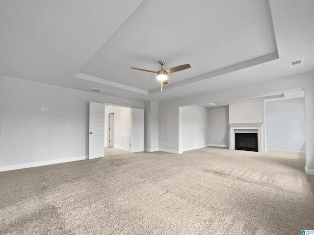 unfurnished living room featuring visible vents, a raised ceiling, ceiling fan, and carpet flooring