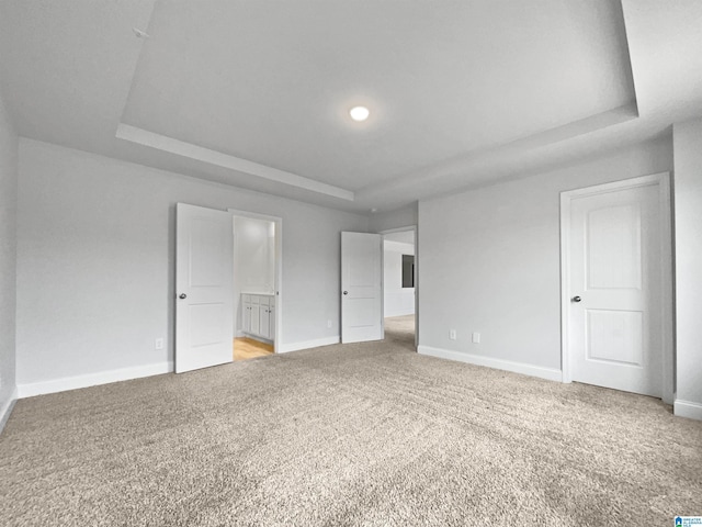 unfurnished bedroom featuring light colored carpet, connected bathroom, a raised ceiling, and baseboards