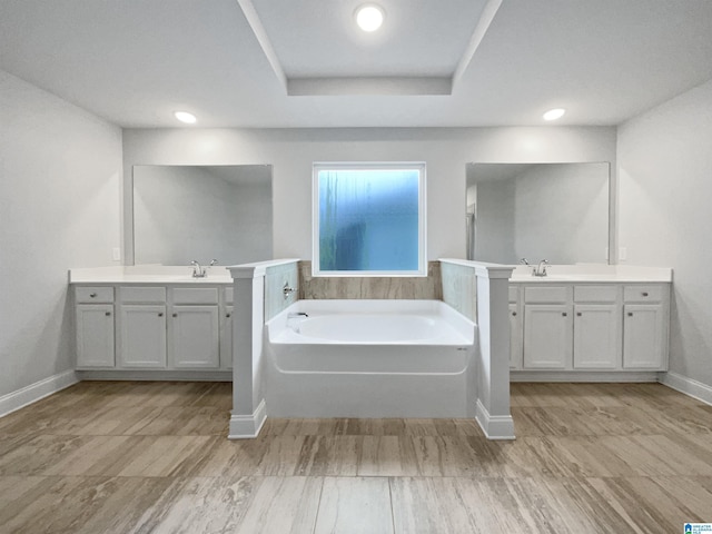 bathroom with baseboards, a tray ceiling, a garden tub, and two vanities