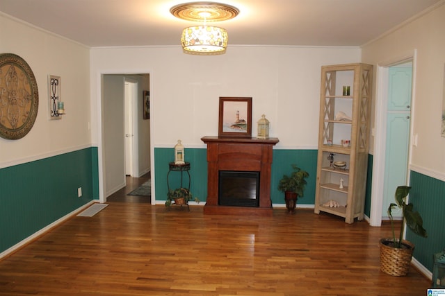 living area with a glass covered fireplace, crown molding, wood finished floors, and wainscoting