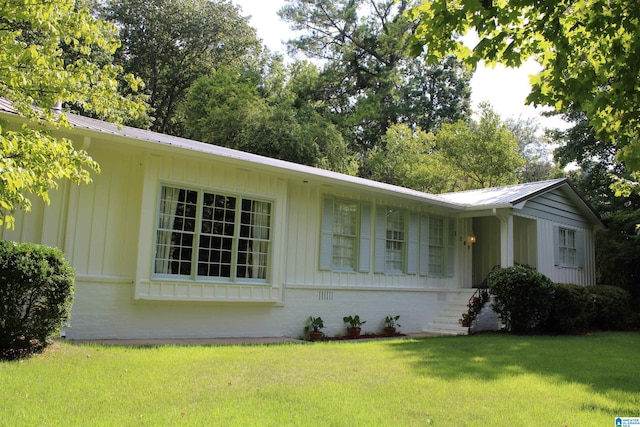 ranch-style house featuring board and batten siding, metal roof, and a front yard