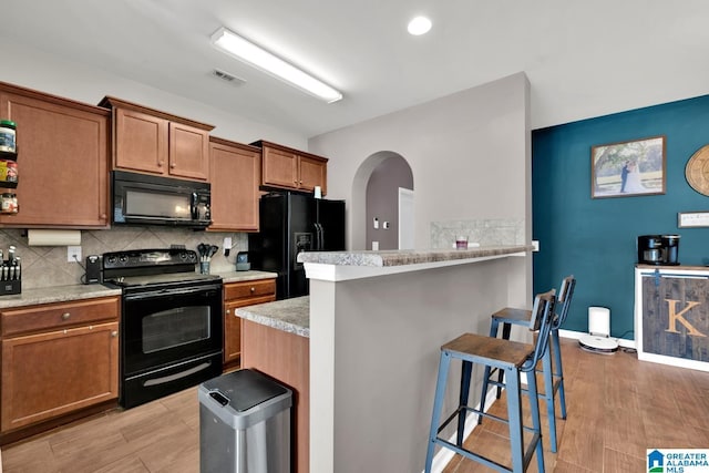 kitchen featuring visible vents, arched walkways, black appliances, light countertops, and a kitchen bar