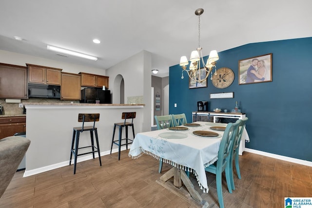 dining area featuring baseboards, arched walkways, an inviting chandelier, and wood finished floors