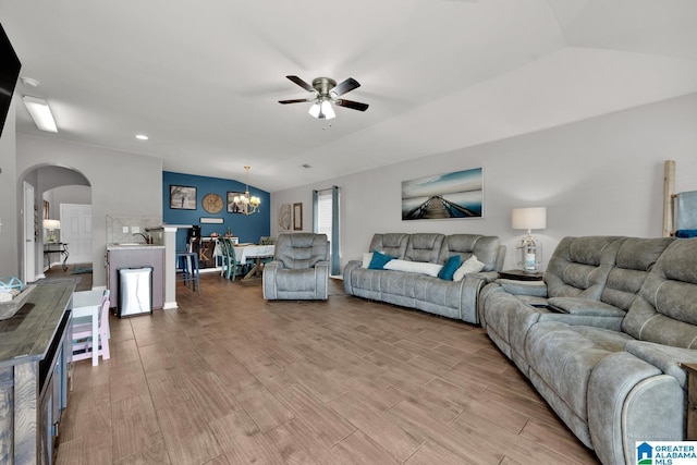 living room with vaulted ceiling, ceiling fan with notable chandelier, arched walkways, and light wood finished floors