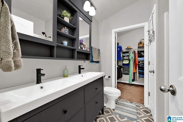 full bath with a walk in closet, toilet, a sink, double vanity, and lofted ceiling