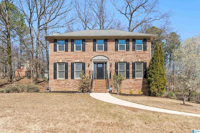 colonial-style house with brick siding, a chimney, and a front lawn