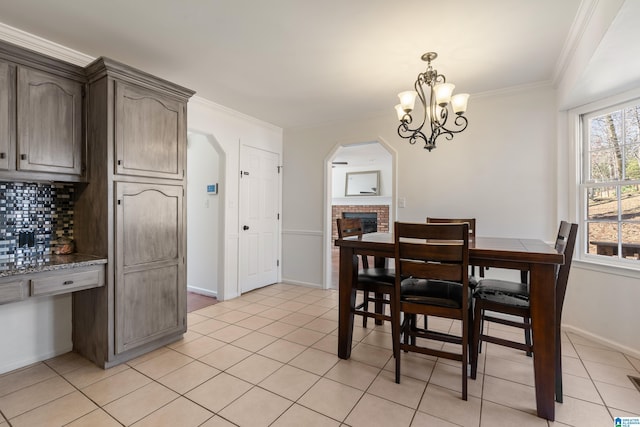 dining room with a brick fireplace, crown molding, baseboards, light tile patterned floors, and an inviting chandelier