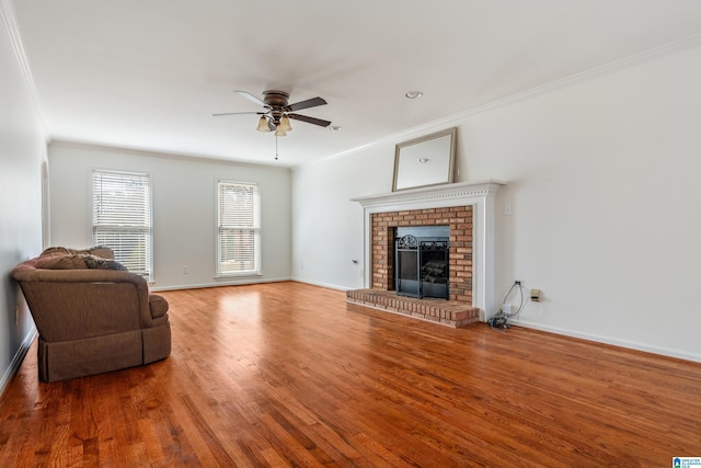 living area with ornamental molding, wood finished floors, baseboards, a brick fireplace, and ceiling fan