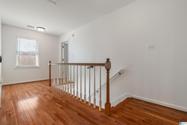 hallway with baseboards, an upstairs landing, visible vents, and hardwood / wood-style flooring