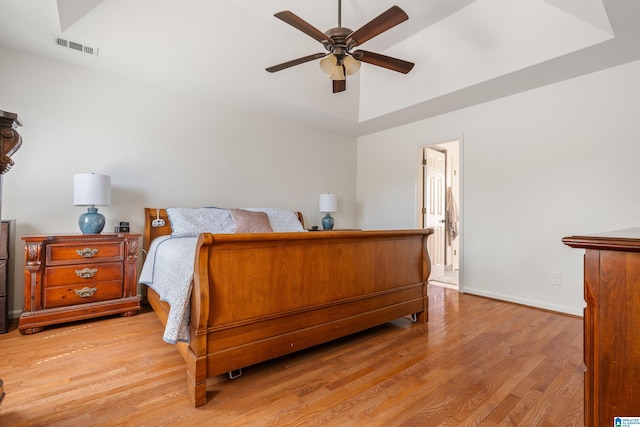 bedroom featuring a tray ceiling, baseboards, visible vents, and light wood finished floors