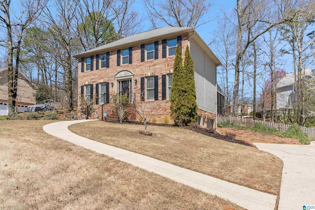 colonial house featuring brick siding, a front yard, and fence