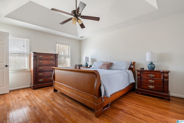 bedroom featuring a raised ceiling, baseboards, light wood-type flooring, and ceiling fan