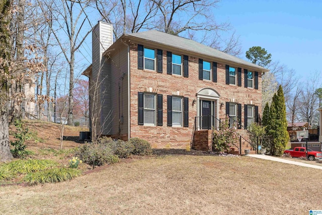 colonial home with a front lawn, central air condition unit, brick siding, and a chimney