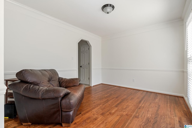 living area featuring crown molding, wood finished floors, arched walkways, and baseboards