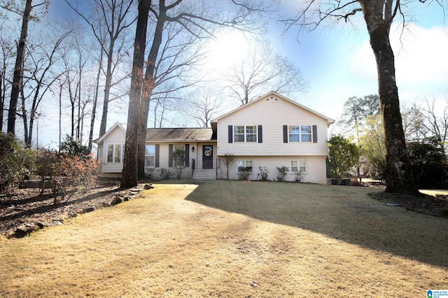 tri-level home featuring a front lawn, brick siding, and dirt driveway