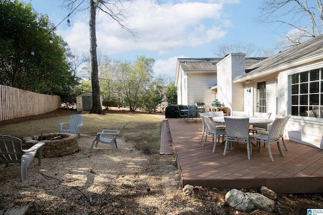 wooden deck featuring fence, an outdoor fire pit, outdoor dining area, an outdoor structure, and a storage unit