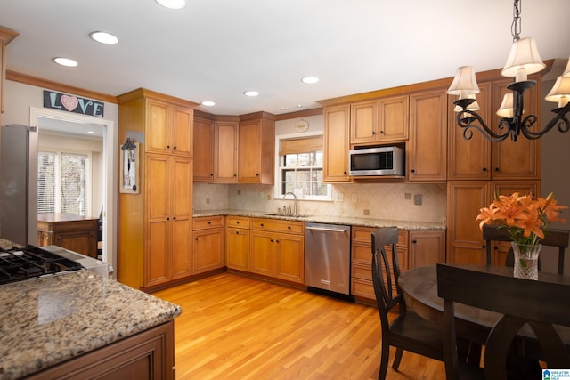 kitchen with light wood finished floors, backsplash, brown cabinets, stainless steel appliances, and a sink