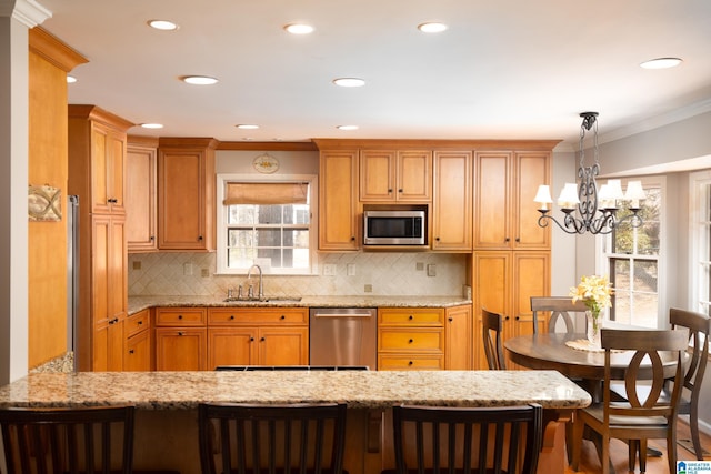 kitchen featuring ornamental molding, a sink, appliances with stainless steel finishes, a peninsula, and light stone countertops