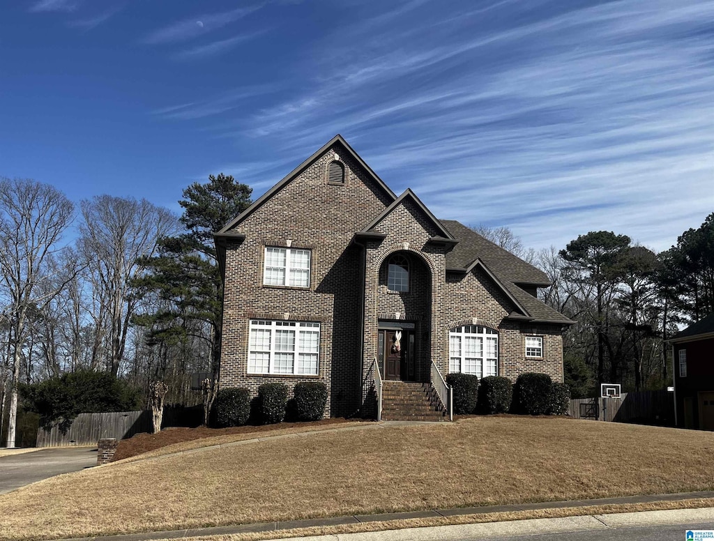 view of front of home with brick siding, a shingled roof, and fence