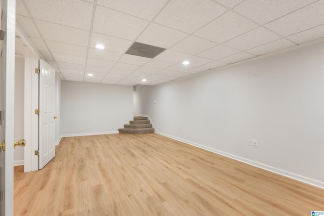 finished below grade area with light wood finished floors, baseboards, stairway, a drop ceiling, and recessed lighting