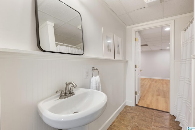 full bathroom featuring baseboards, a drop ceiling, and a sink