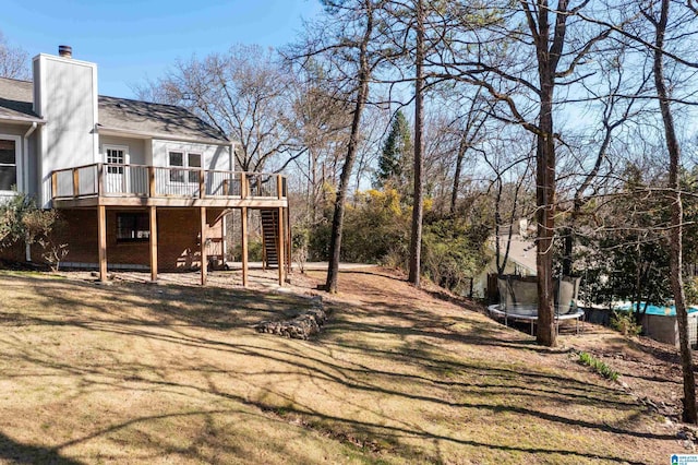 view of yard featuring a wooden deck, a trampoline, and stairs