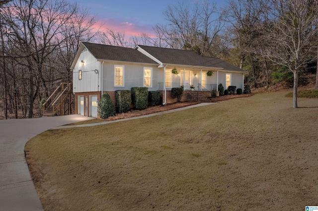 view of front facade featuring a front lawn, concrete driveway, stairs, covered porch, and an attached garage