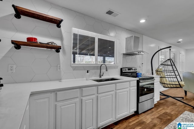 kitchen with wood finished floors, stainless steel electric range, a sink, wall chimney exhaust hood, and tasteful backsplash