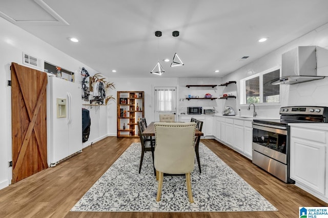 kitchen featuring visible vents, stainless steel range with electric stovetop, wood finished floors, white fridge with ice dispenser, and wall chimney exhaust hood