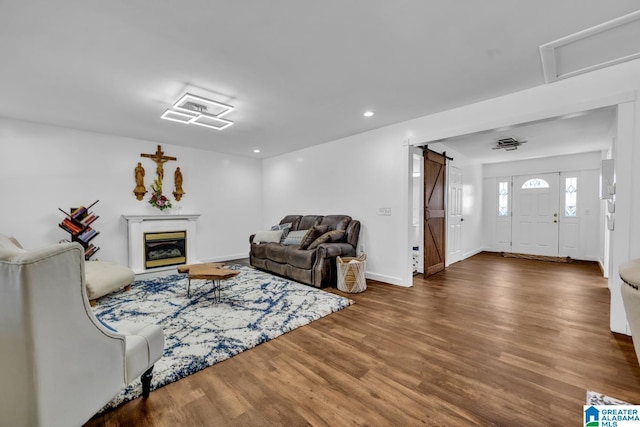 living area featuring baseboards, a barn door, recessed lighting, wood finished floors, and a glass covered fireplace