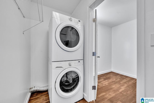 laundry room featuring laundry area, stacked washer and clothes dryer, baseboards, and wood finished floors