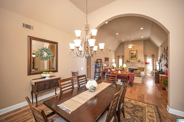 dining area featuring visible vents, ceiling fan with notable chandelier, wood finished floors, arched walkways, and a fireplace