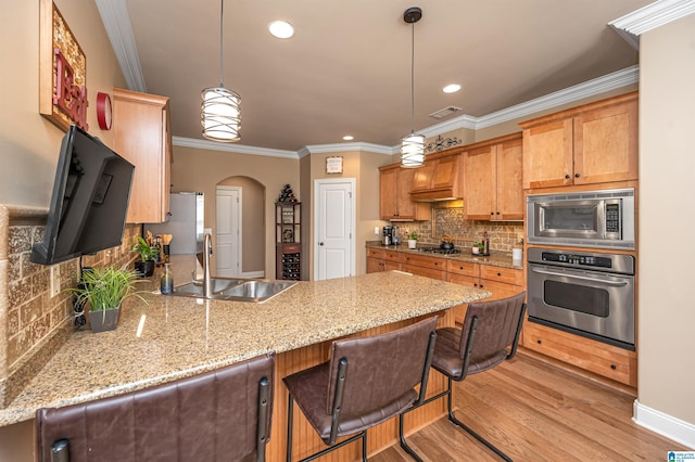 kitchen with crown molding, appliances with stainless steel finishes, a peninsula, light wood-style floors, and a sink