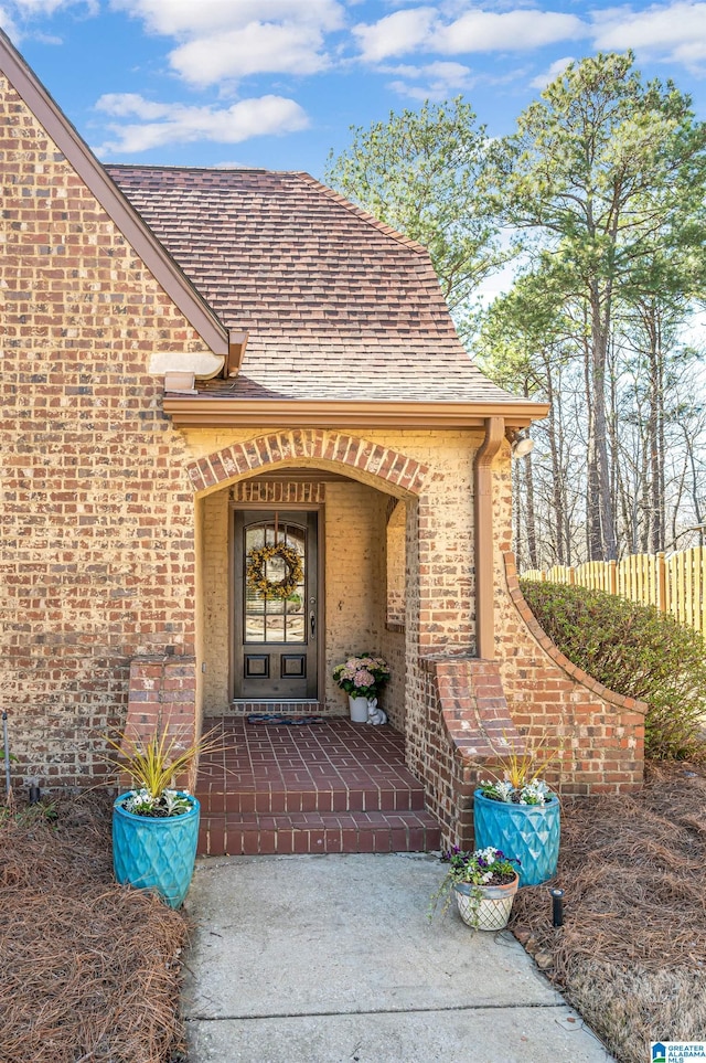 property entrance with fence, brick siding, and roof with shingles