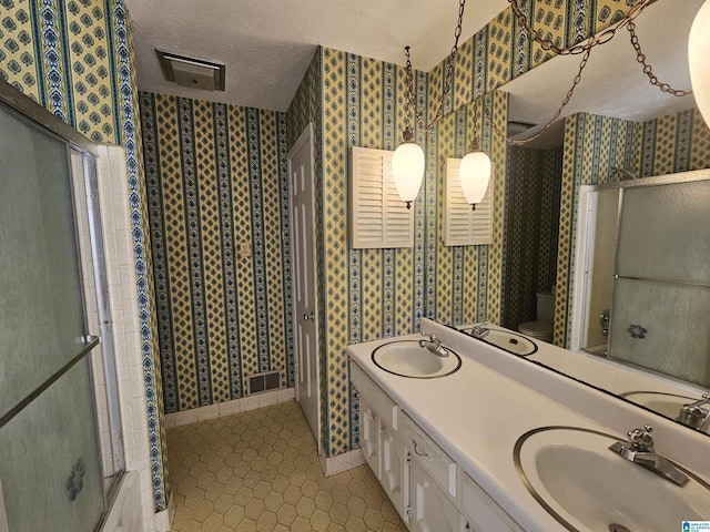 bathroom featuring a sink, a textured ceiling, tile patterned floors, and wallpapered walls