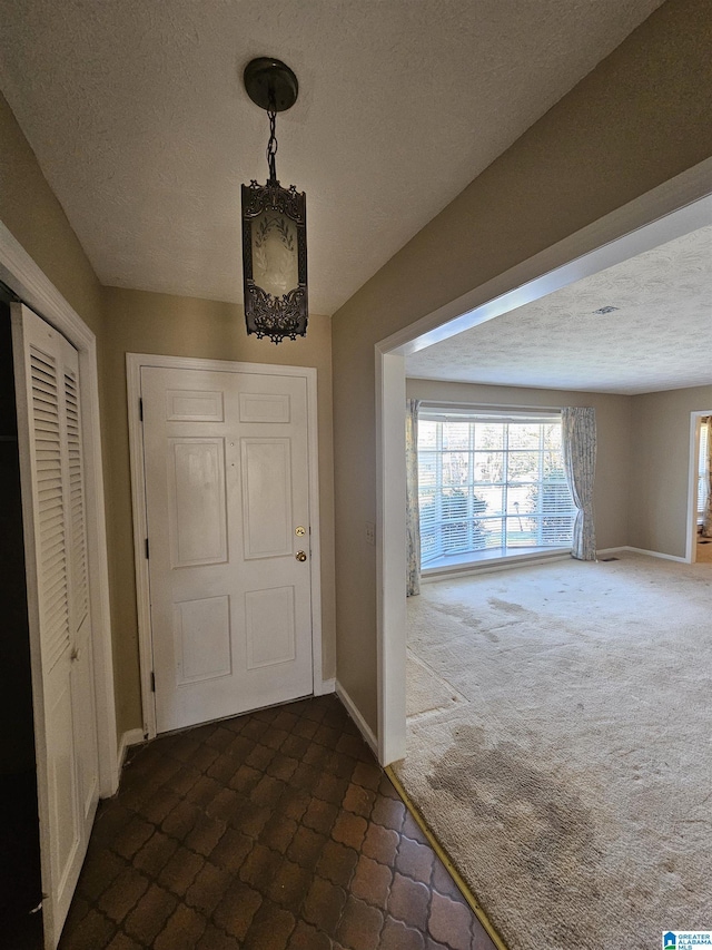 foyer entrance featuring baseboards, dark carpet, and a textured ceiling