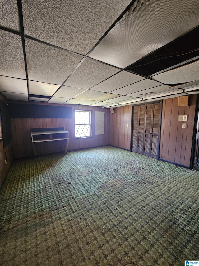 interior space featuring a drop ceiling and wooden walls