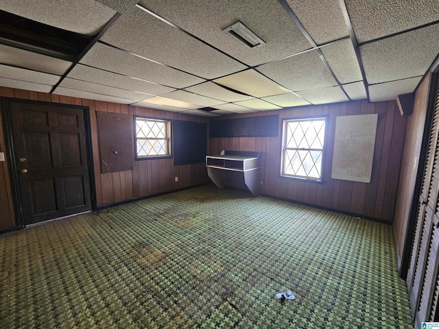 empty room with wooden walls, a drop ceiling, and a wealth of natural light