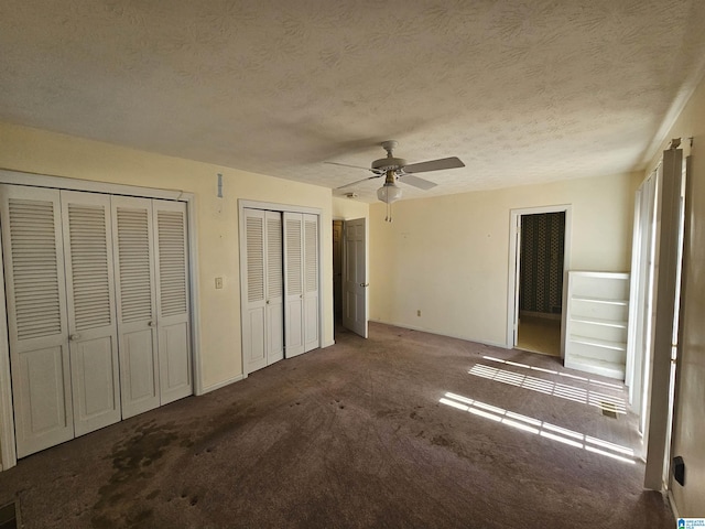 unfurnished bedroom with multiple closets, carpet, a ceiling fan, and a textured ceiling