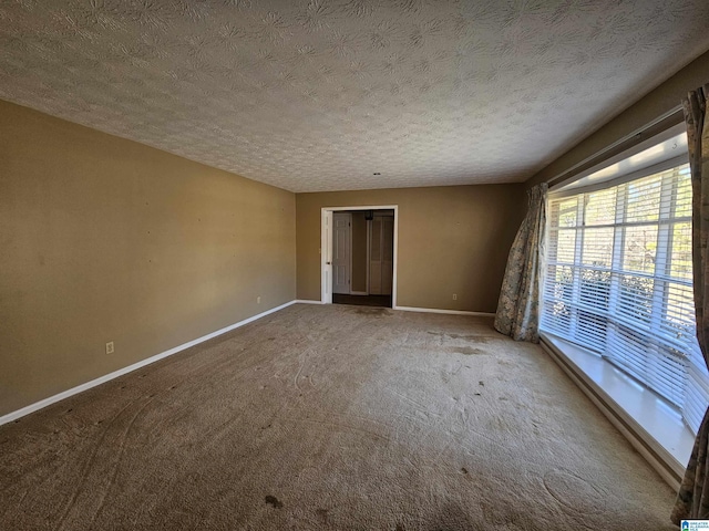 carpeted spare room featuring a textured ceiling and baseboards