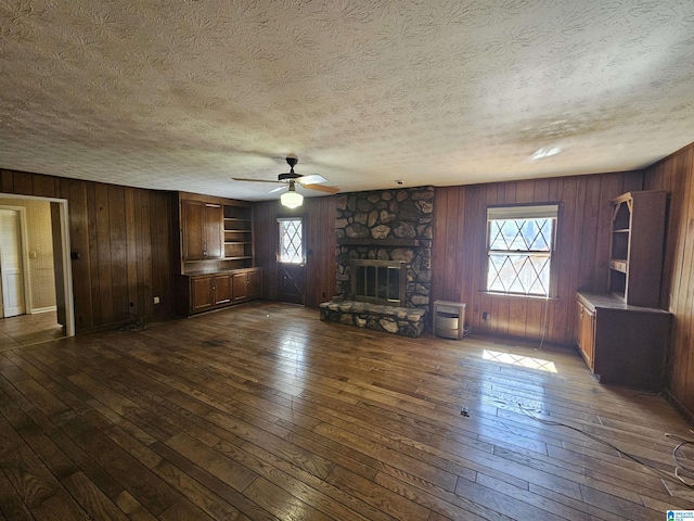 unfurnished living room with a healthy amount of sunlight, a fireplace, a ceiling fan, and dark wood-style flooring