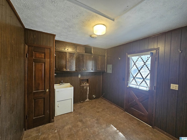 washroom with a sink, cabinet space, wooden walls, and a textured ceiling