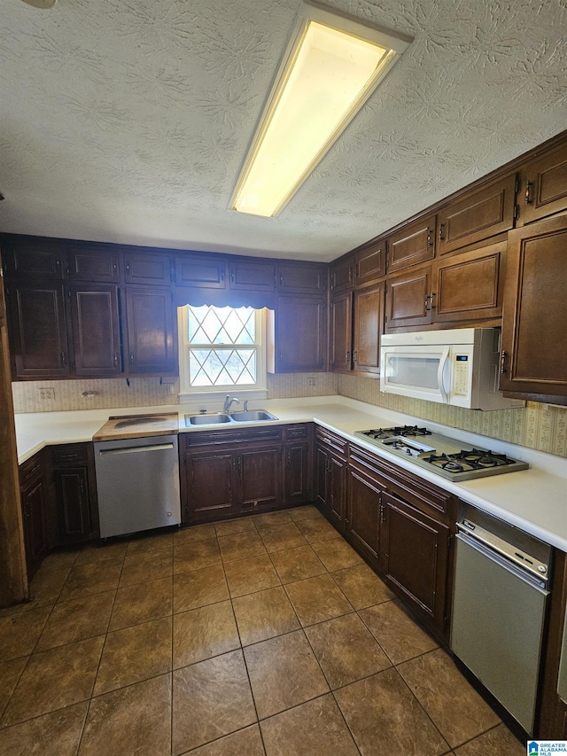 kitchen featuring dark tile patterned floors, a sink, a textured ceiling, white appliances, and light countertops